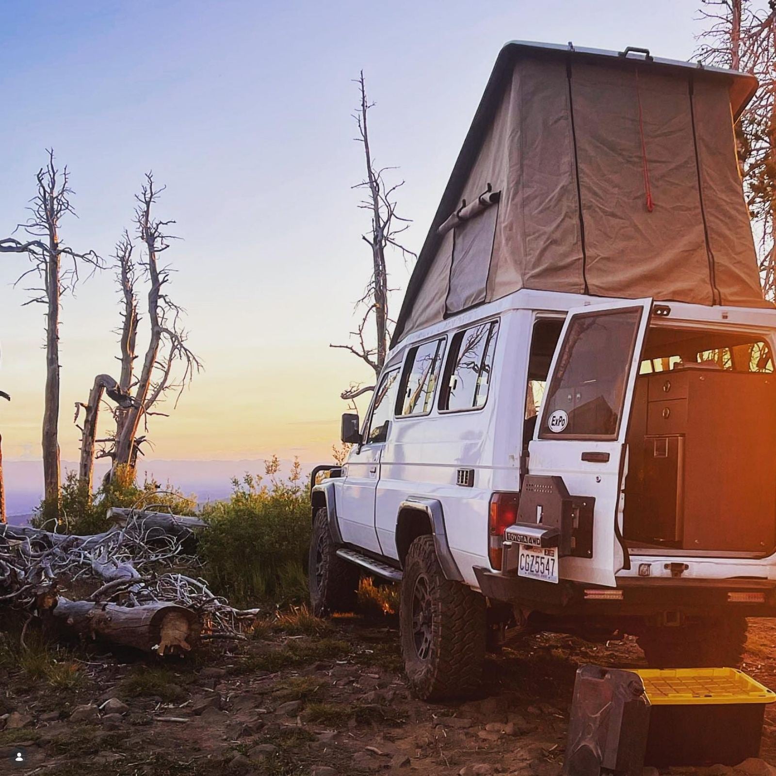 White Toyota Troopy with the roof tent up and the back open at a ridgeline camp at sunset