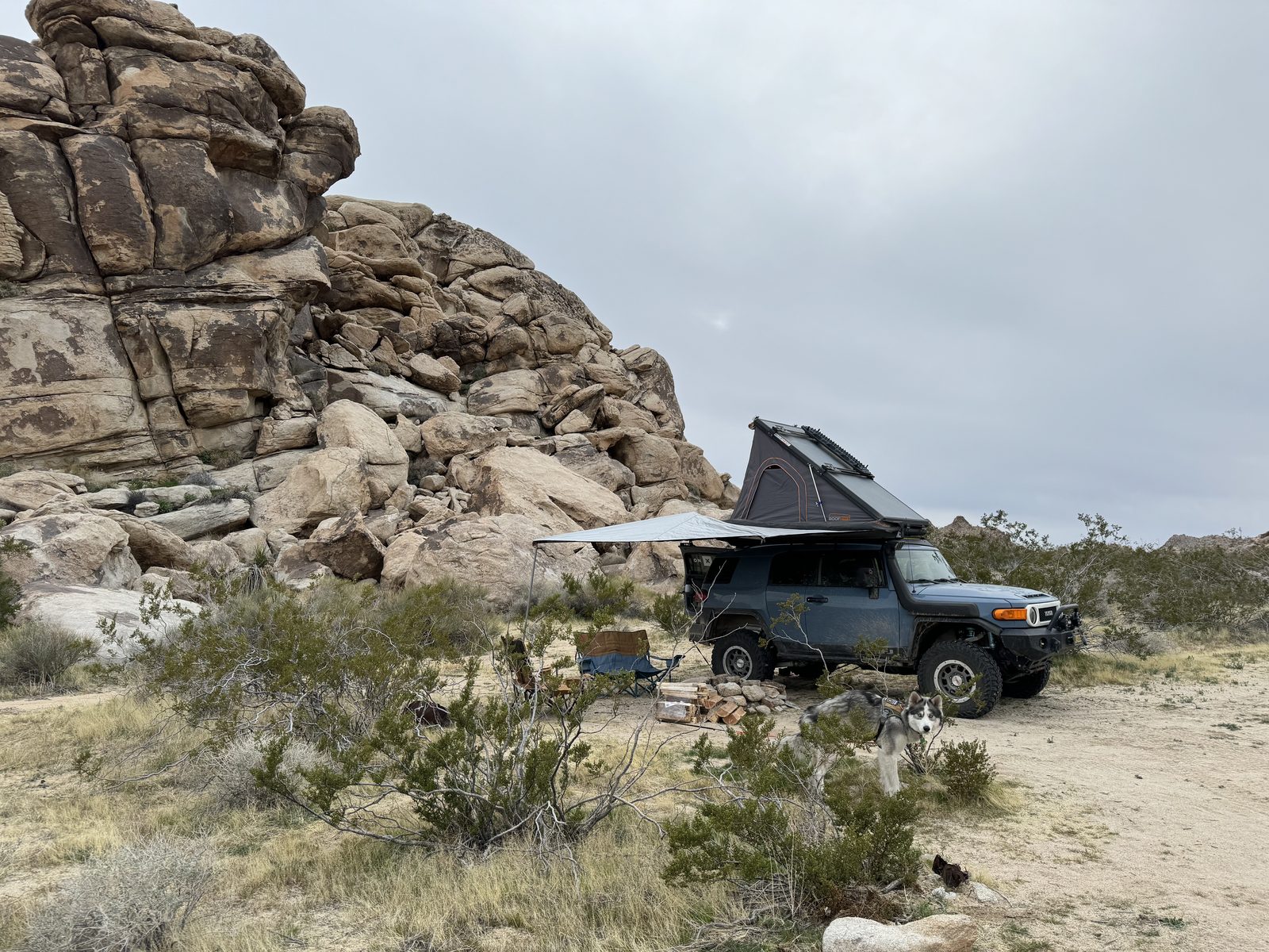 The FJ with its tent up beside granite boulders under clouds